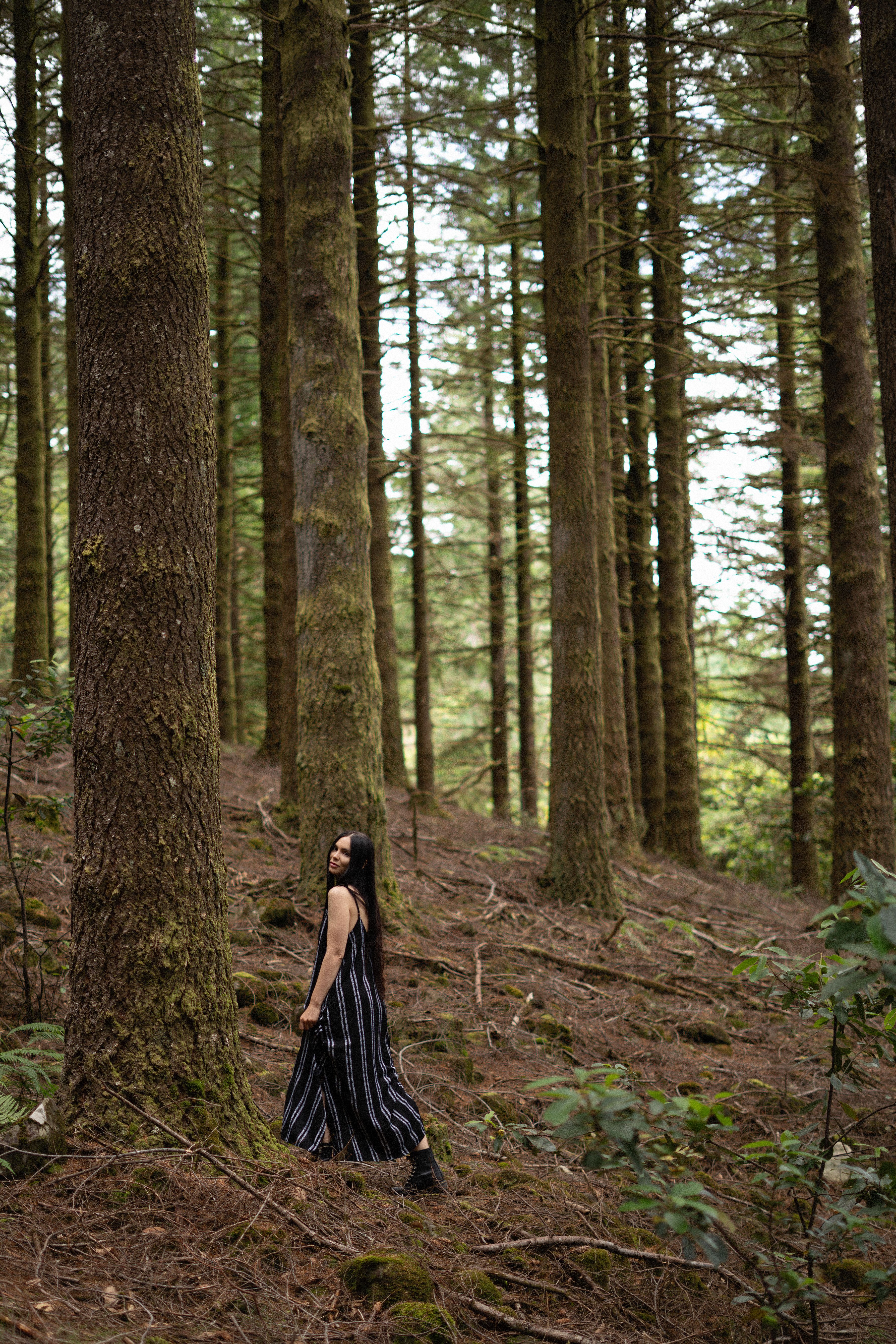 Frau im dunklen Kleid geht durch einen Wald