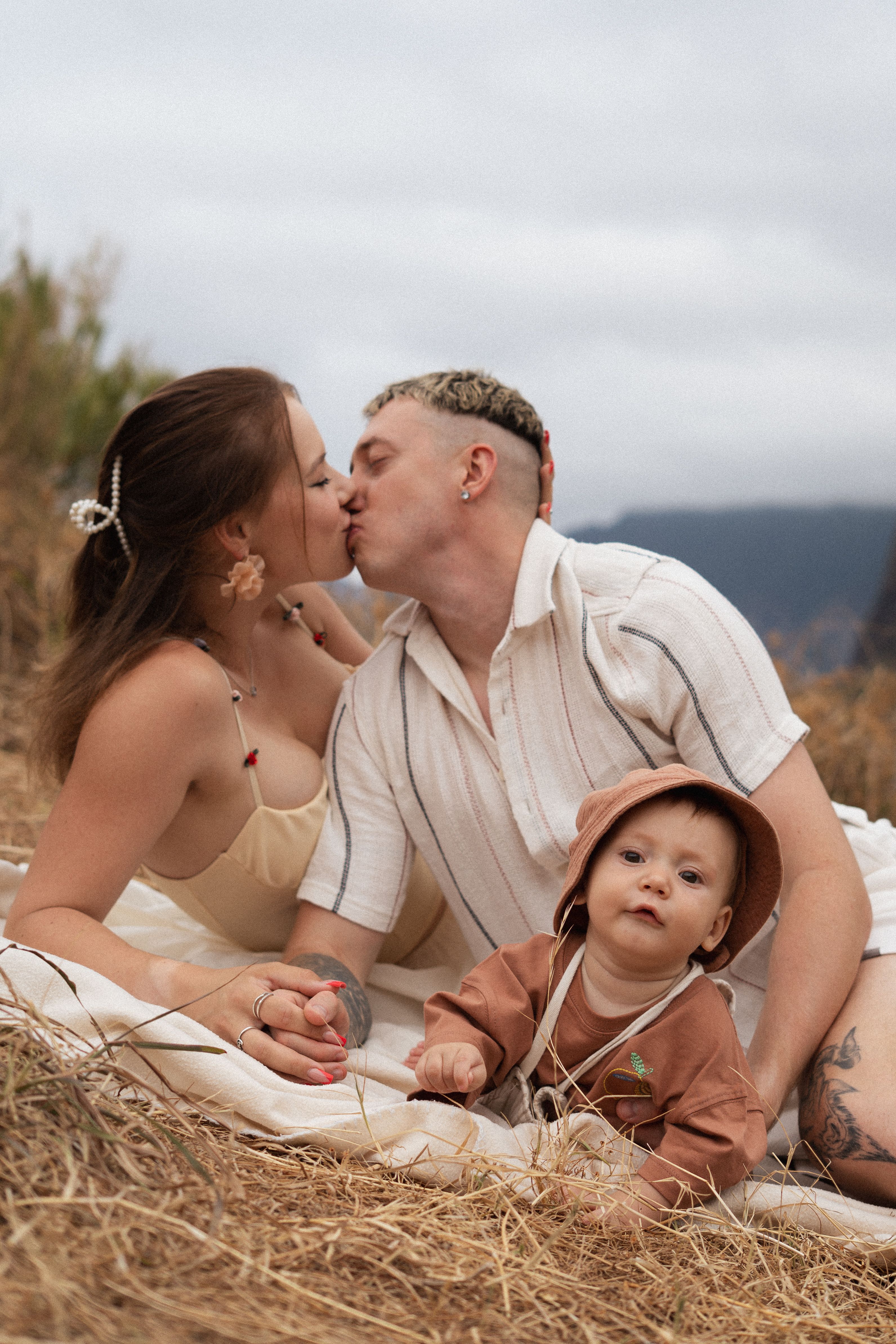 Eltern küssen sich neben ihrem Baby auf einer Decke im hohen Gras